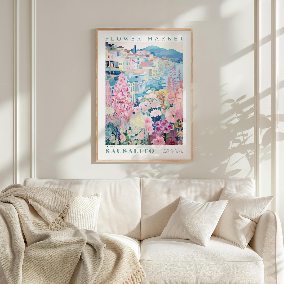 a framed poster of a colorful floral scene hanging on a wall above a white couch with a blanket draped over it.