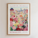 A framed poster depicting a vibrant flower market in Kansas City, with a cityscape in the background.