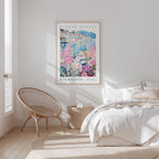 a bedroom with a bed, a woven chair, and a framed poster of a colorful floral scene hanging on the wall.