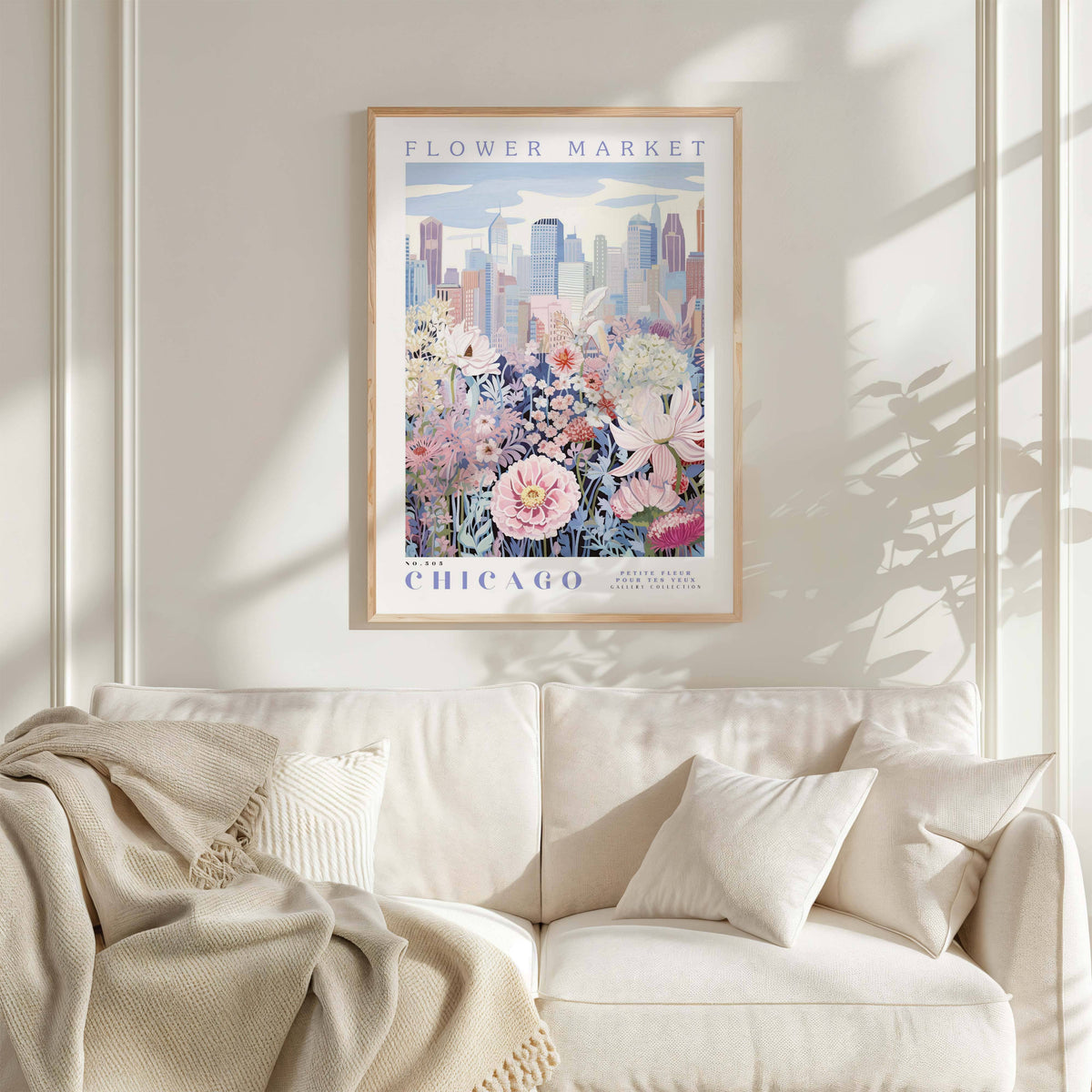 a framed poster of a cityscape with a flower market in Chicago, hanging on a wall above a white couch with a blanket draped over it.