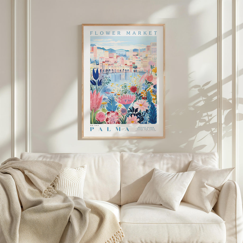 a framed poster of a colorful floral scene hanging on a wall above a white couch with a blanket draped over it.