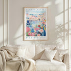 a framed poster of a colorful floral scene hanging on a wall above a white couch with a blanket draped over it.