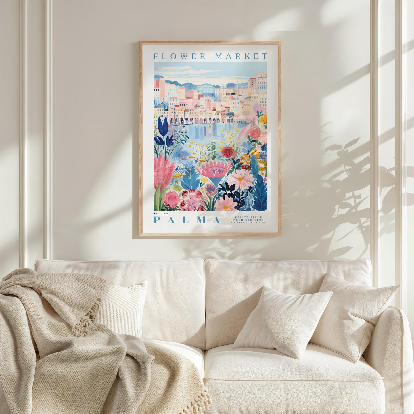 a framed poster of a colorful floral scene hanging on a wall above a white couch with a blanket draped over it.