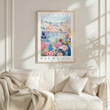 a framed poster of a colorful floral scene hanging on a wall above a white couch with a blanket draped over it.