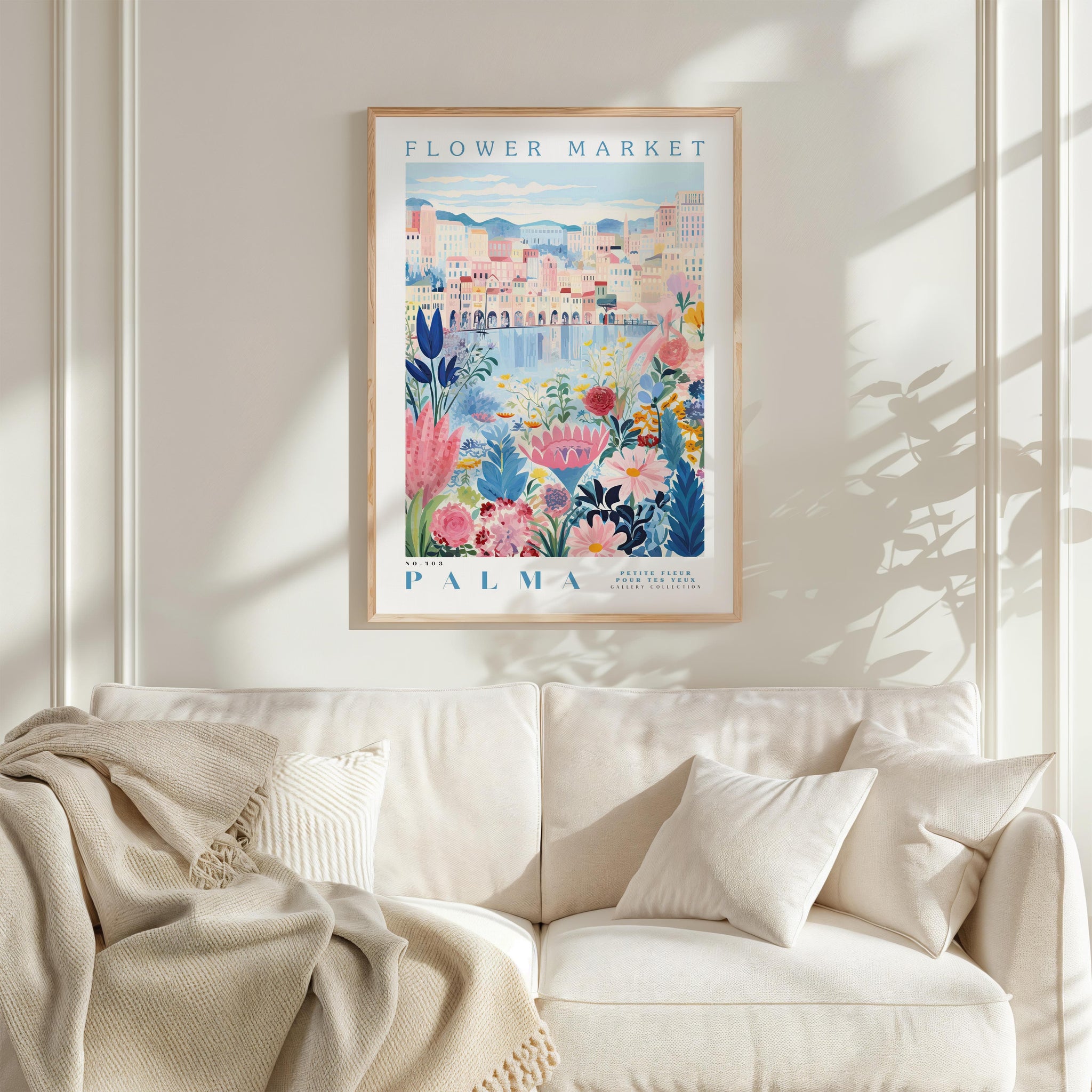 a framed poster of a colorful floral scene hanging on a wall above a white couch with a blanket draped over it.