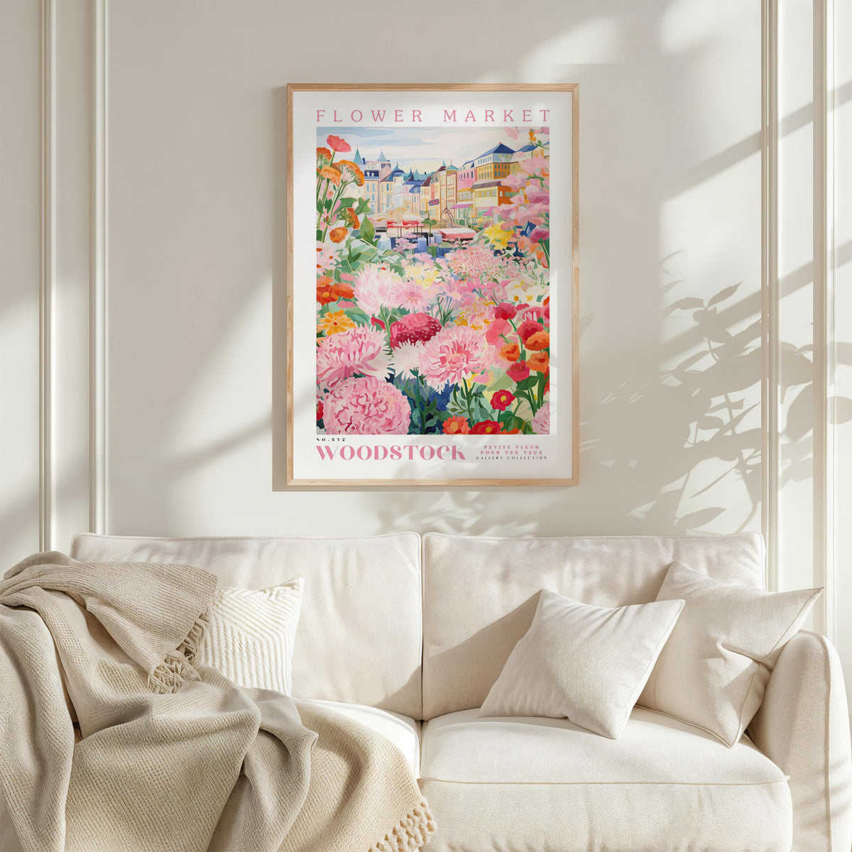 a framed poster of a vibrant floral scene hanging on a wall above a white couch with a blanket draped over it.