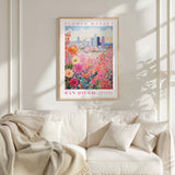a framed poster of a colorful floral scene hanging on a wall above a white couch with a blanket draped over it.