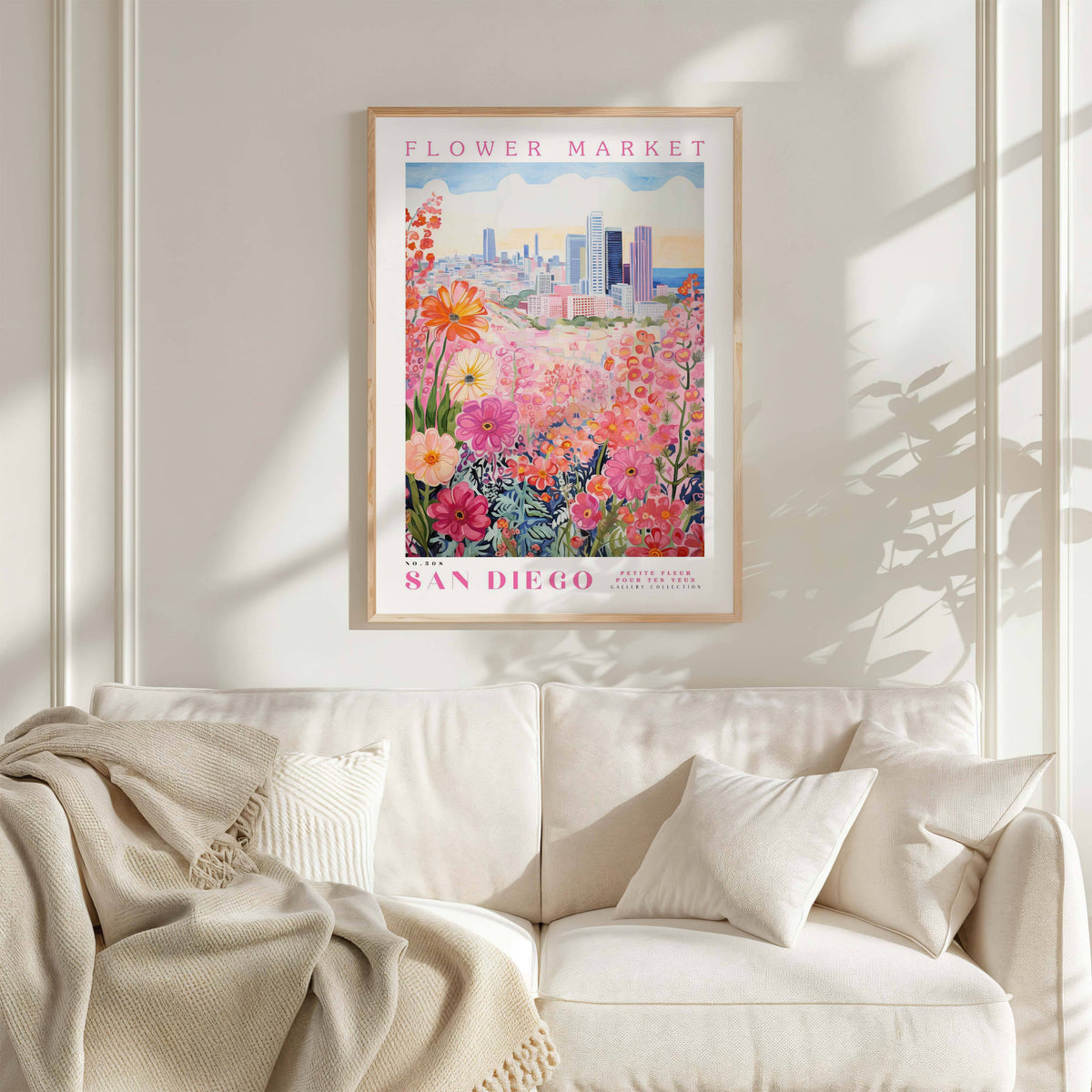 a framed poster of a colorful floral scene hanging on a wall above a white couch with a blanket draped over it.
