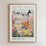 The image is a framed poster depicting a vibrant and colorful flower market in the city of Arlington, with a variety of flowers and plants in the foreground and a cityscape in the background.