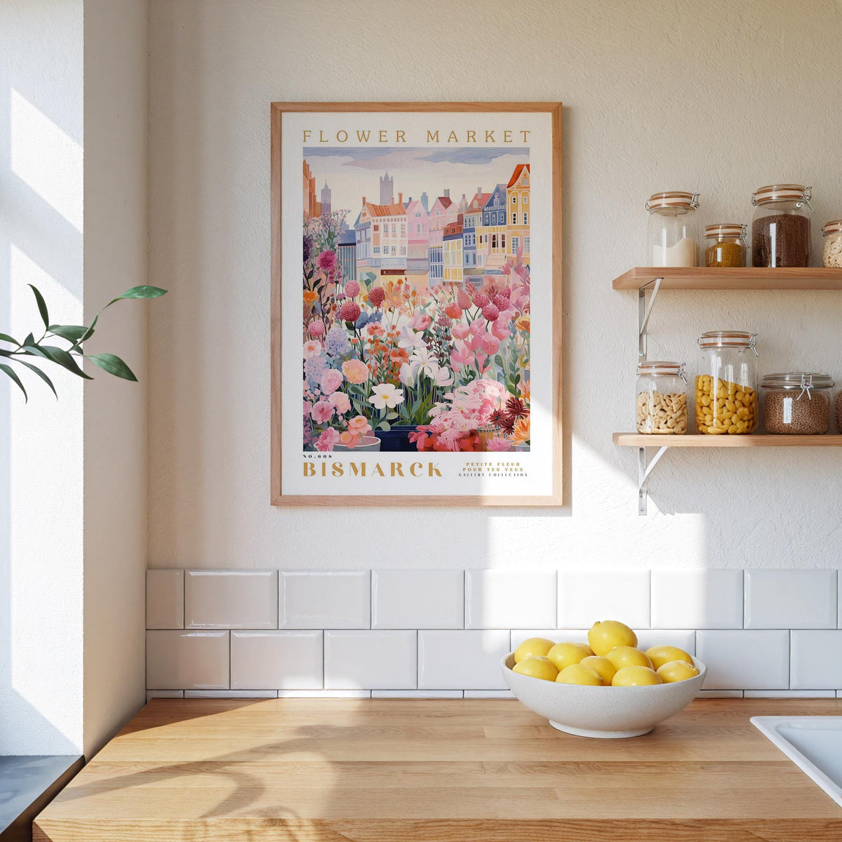 a kitchen scene with a framed poster of a flower market hanging on the wall above a wooden counter. On the counter, there is a bowl of lemons and a plant. The kitchen has white tile walls and a wooden floor.