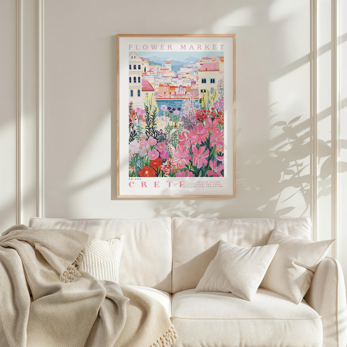 a framed poster of a colorful floral scene hanging on a wall above a white couch with a blanket draped over it.