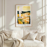 a framed poster of a scenic landscape with a yellow and orange background, depicting a mountain range and a river. The poster is hanging on a wall above a white couch, which has a blanket draped over it.