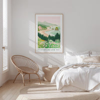 a serene bedroom scene with a large framed poster of a coastal landscape hanging on the wall, a woven chair, and a neatly made bed with white linens.