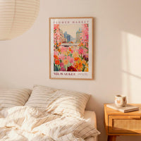 a bedroom setting with a framed poster of a colorful floral scene hanging on the wall above a bed with striped pillows.