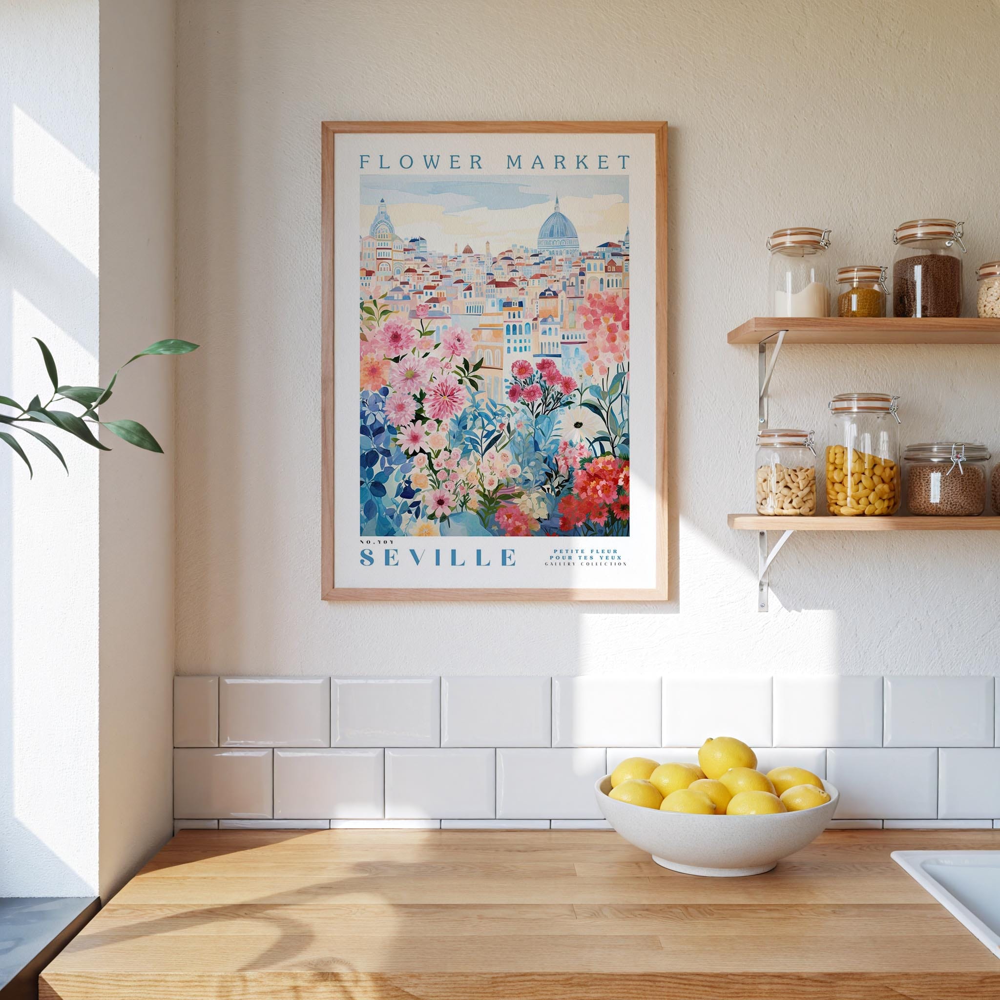 a kitchen scene with a framed poster of the "Flower Market" in Seville hanging on the wall above a wooden counter. On the counter, there is a bowl of lemons and a plant. The kitchen has white tile backsplash and shelves with various jars and containers.