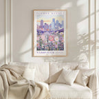 a framed poster of a cityscape with a field of flowers in the foreground, hanging on a wall above a white couch.