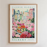 A framed poster depicting a vibrant flower market in a city, with colorful flowers and buildings in the background.