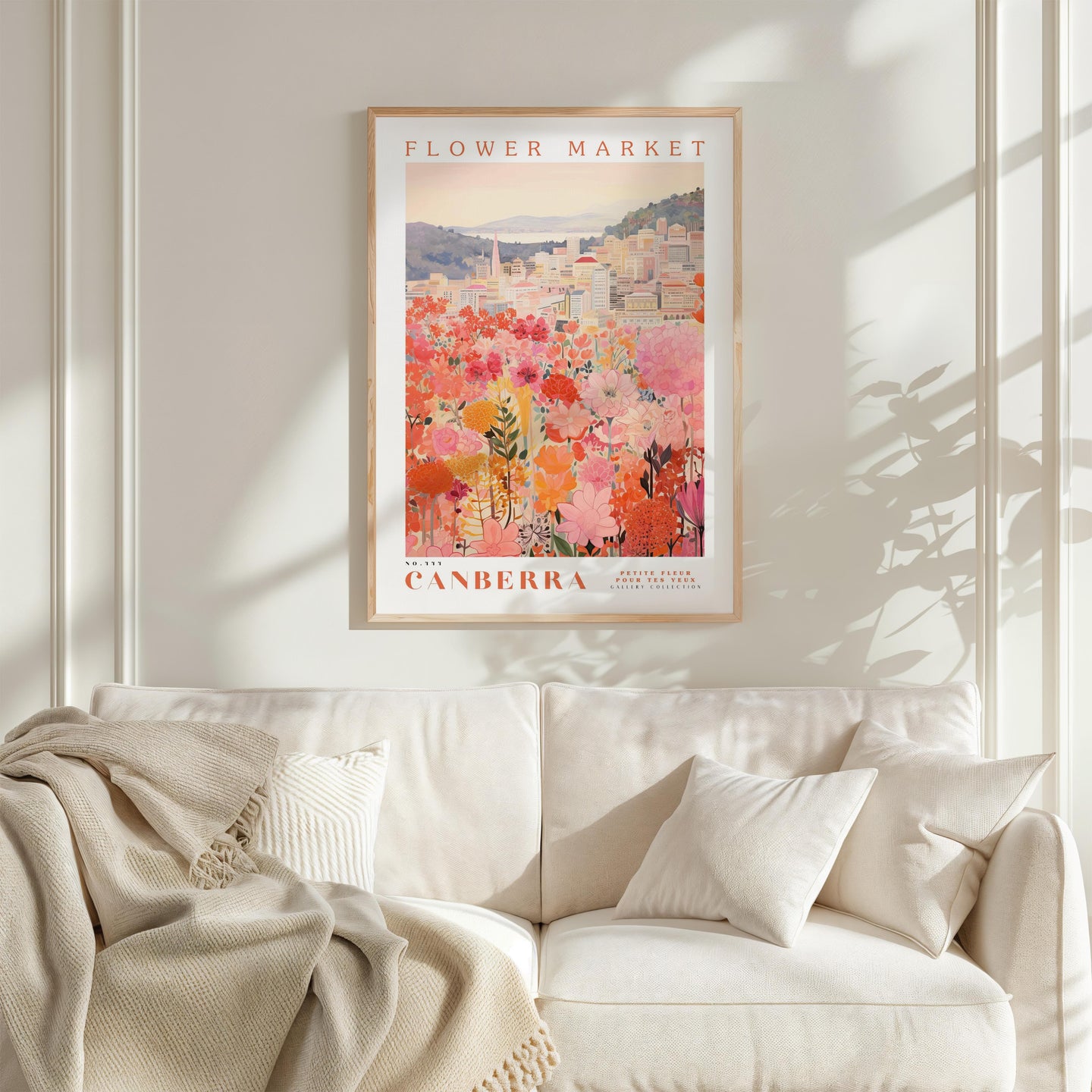 a framed poster of a flower market in Australia hanging on a wall above a white couch with a blanket draped over it.