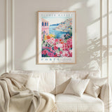 a framed poster of a colorful floral scene hanging on a wall above a white couch with a blanket draped over it.