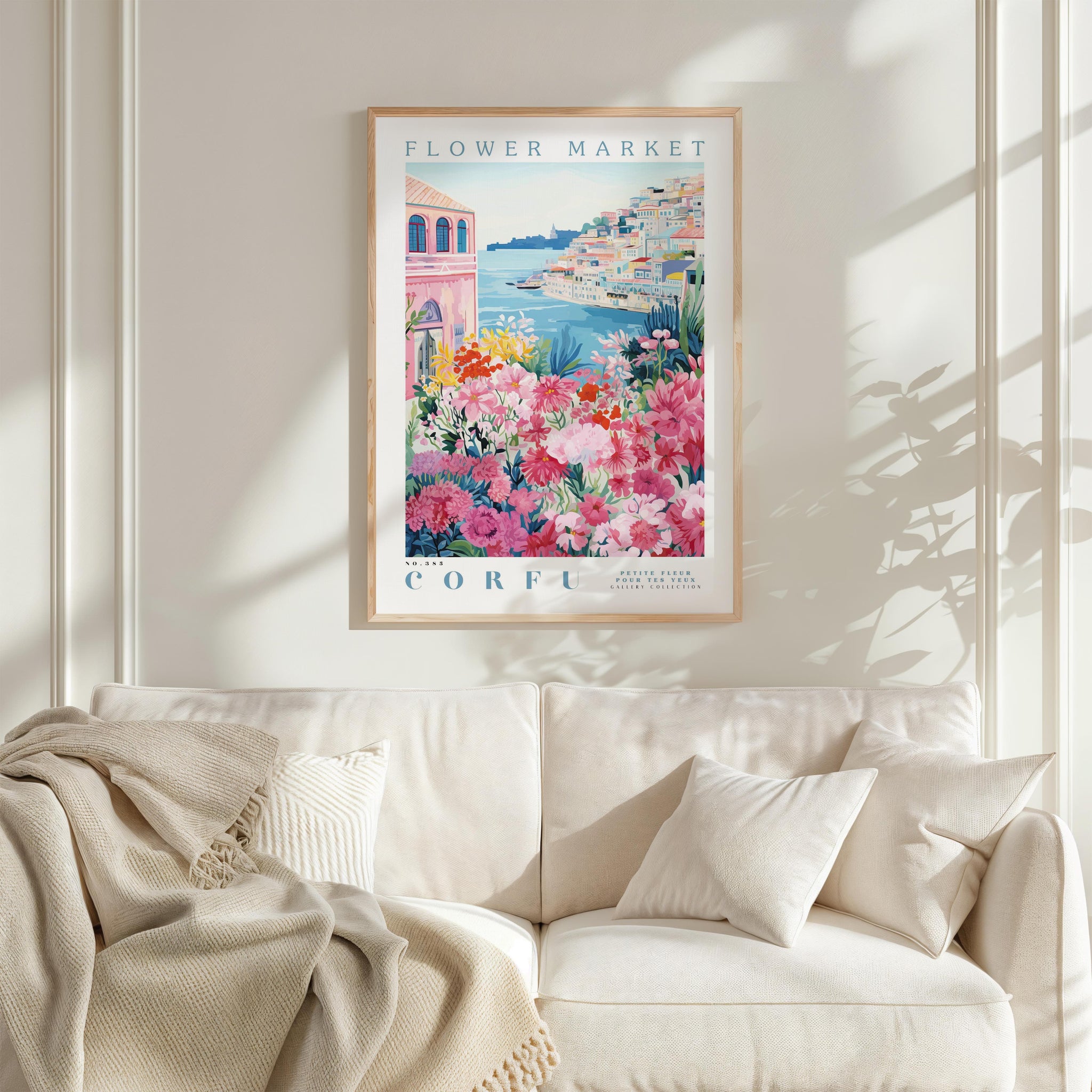 a framed poster of a colorful floral scene hanging on a wall above a white couch with a blanket draped over it.