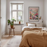 a cozy bedroom with a large bed, a nightstand with a potted plant, and a framed poster of a cityscape on the wall.