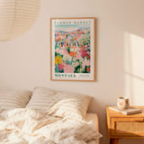 a bedroom scene with a framed poster of a flower market hanging on the wall above a bed with striped pillows.