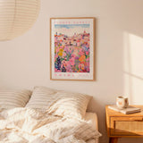 a bedroom scene with a framed poster of a colorful cityscape hanging on the wall above a bed with striped pillows.