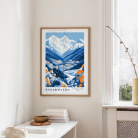 a framed poster of a mountainous landscape with a river, hanging on a wall in a room with a white table and a window.