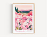 A framed poster depicting a scenic landscape with a field of pink flowers, mountains in the background, and a bridge in the distance.