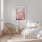 a bedroom with a bed, a woven chair, and a framed poster of a cityscape with flowers hanging on the wall.
