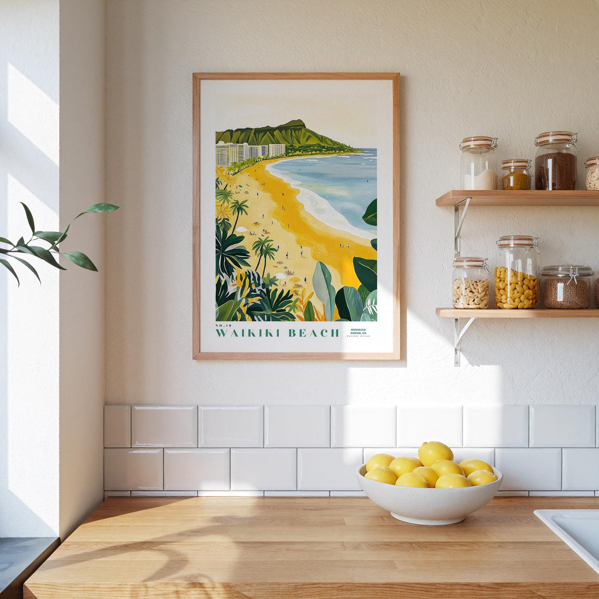 a framed poster of Waikiki Beach hanging on a wall above a kitchen counter with a bowl of lemons on it.