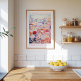 a kitchen scene with a framed poster of a colorful flower market in Phoenix hanging on the wall above a wooden counter. On the counter, there is a bowl of lemons and a plant.