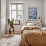 A cozy bedroom with a large bed, a nightstand with a plant, and a framed poster of a cityscape on the wall.