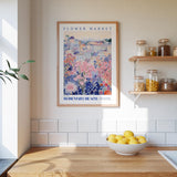 a kitchen scene with a framed poster of a colorful floral scene hanging on the wall above a wooden countertop with a bowl of lemons.