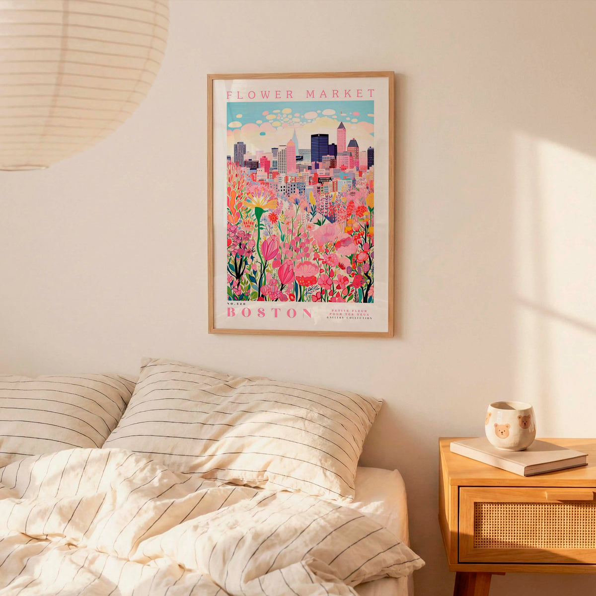 a framed poster of a cityscape with a flower market in the background, hanging on a wall above a bed with striped pillows.