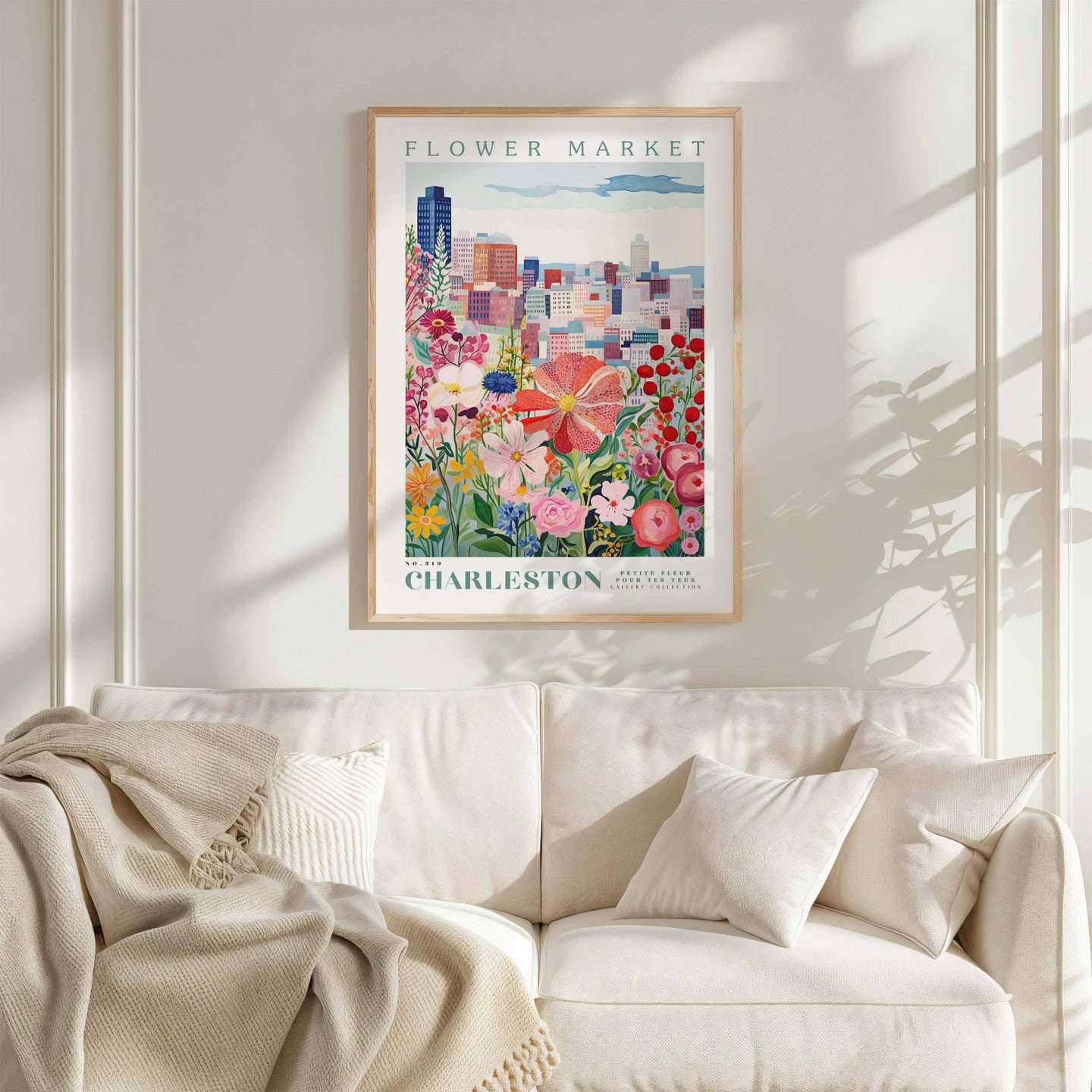 a framed poster of a colorful cityscape with flowers, hanging on a wall above a white couch with pillows.