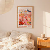 a bedroom scene with a framed poster of a colorful flower market hanging on the wall above a bed with striped pillows.
