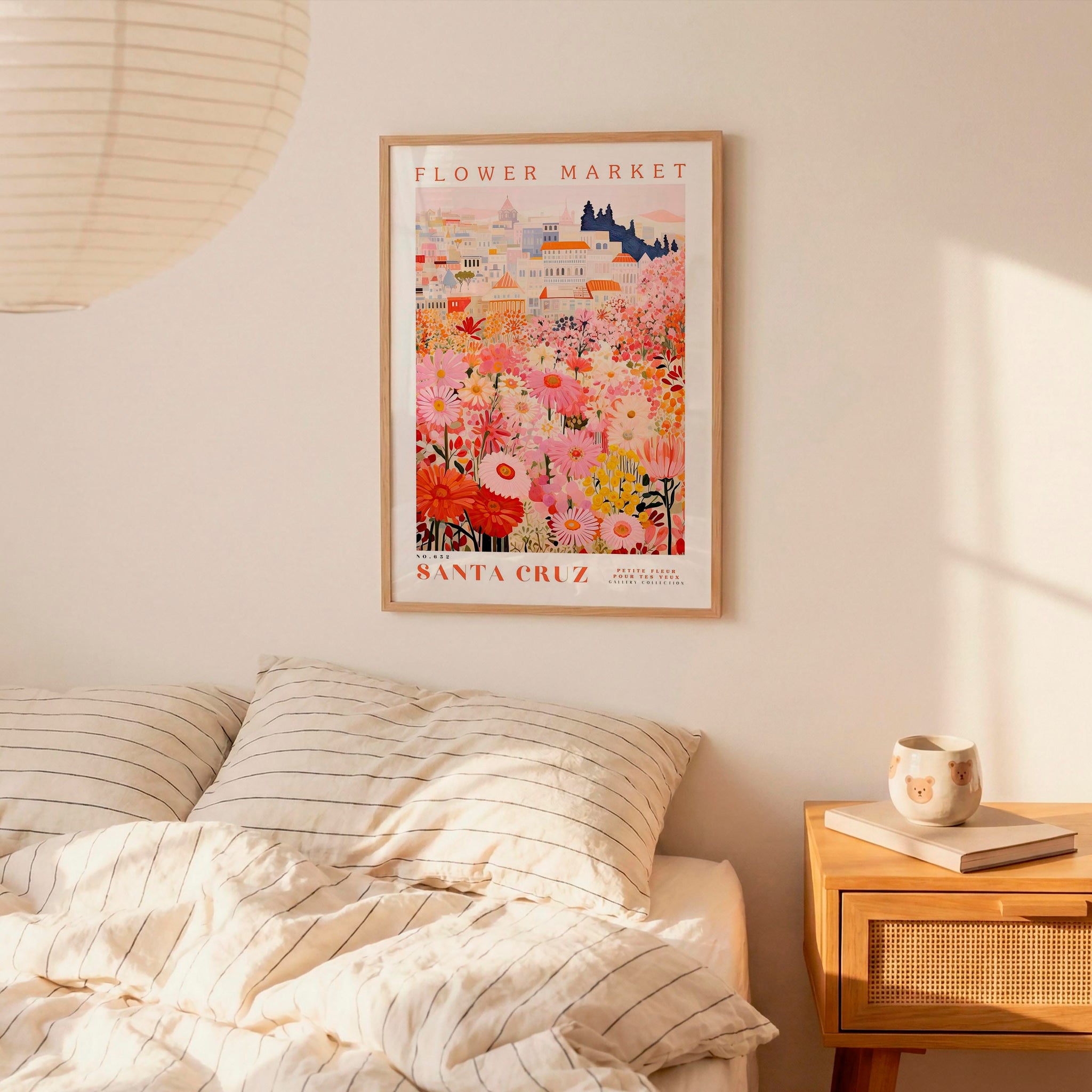 a bedroom scene with a framed poster of a colorful flower market hanging on the wall above a bed with striped pillows.