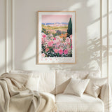 a framed poster of a garden with pink flowers hanging on a wall above a white couch with pillows.