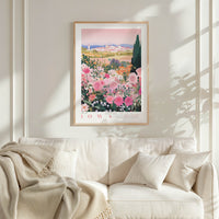 a framed poster of a garden with pink flowers hanging on a wall above a white couch with pillows.