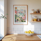 a framed poster of a cityscape with flowers hanging on a wall above a wooden table with a bowl of lemons.