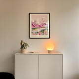 a white cabinet with a framed picture of a mountain landscape hanging above it, and a small lamp on the cabinet.