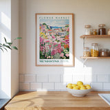 a framed poster of a flower market in Mendocino, California, hanging on a wall above a kitchen counter with a bowl of lemons.