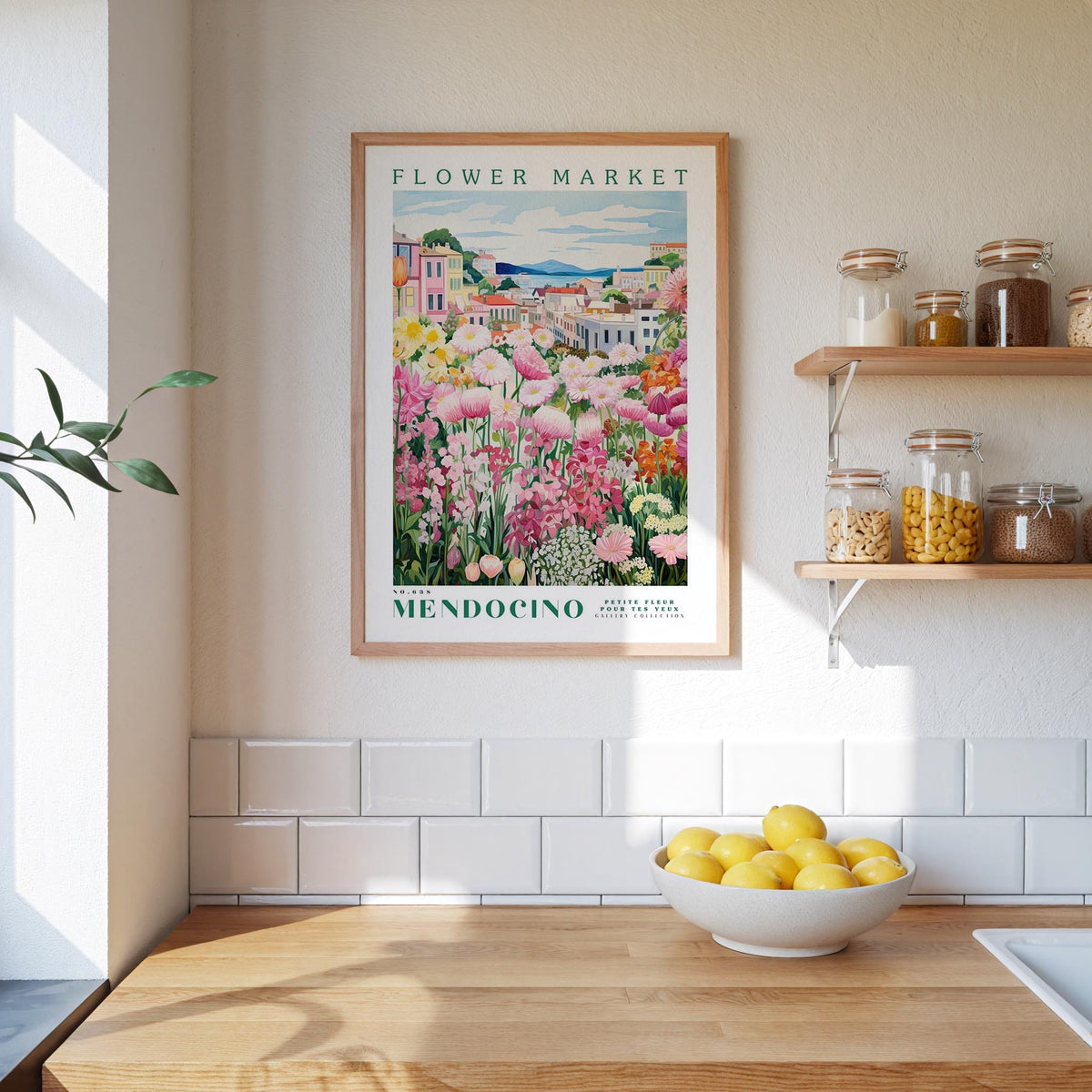 a framed poster of a flower market in Mendocino, California, hanging on a wall above a kitchen counter with a bowl of lemons.