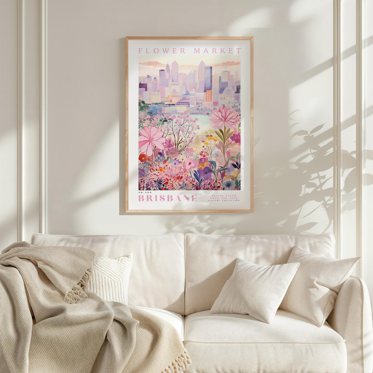 a framed poster of a cityscape with flowers, hanging on a wall above a white couch with pillows.