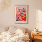 a bedroom scene with a framed poster of a colorful flower market hanging on the wall above a bed with striped pillows.