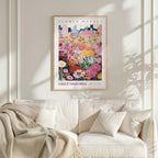 a framed poster of a colorful floral scene hanging on a wall above a white couch with pillows.