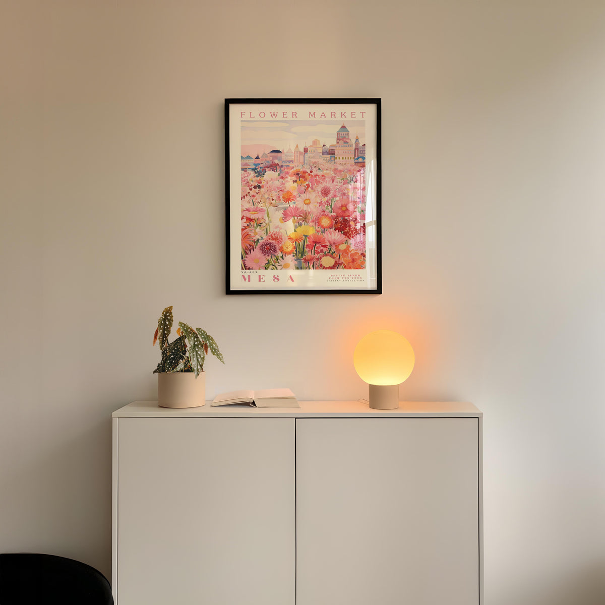 a white cabinet with a potted plant and a lamp on top, set against a wall with a framed poster of a cityscape above it.