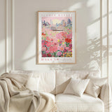 a framed poster of a cityscape with a field of flowers in the foreground, hanging on a wall above a white couch.