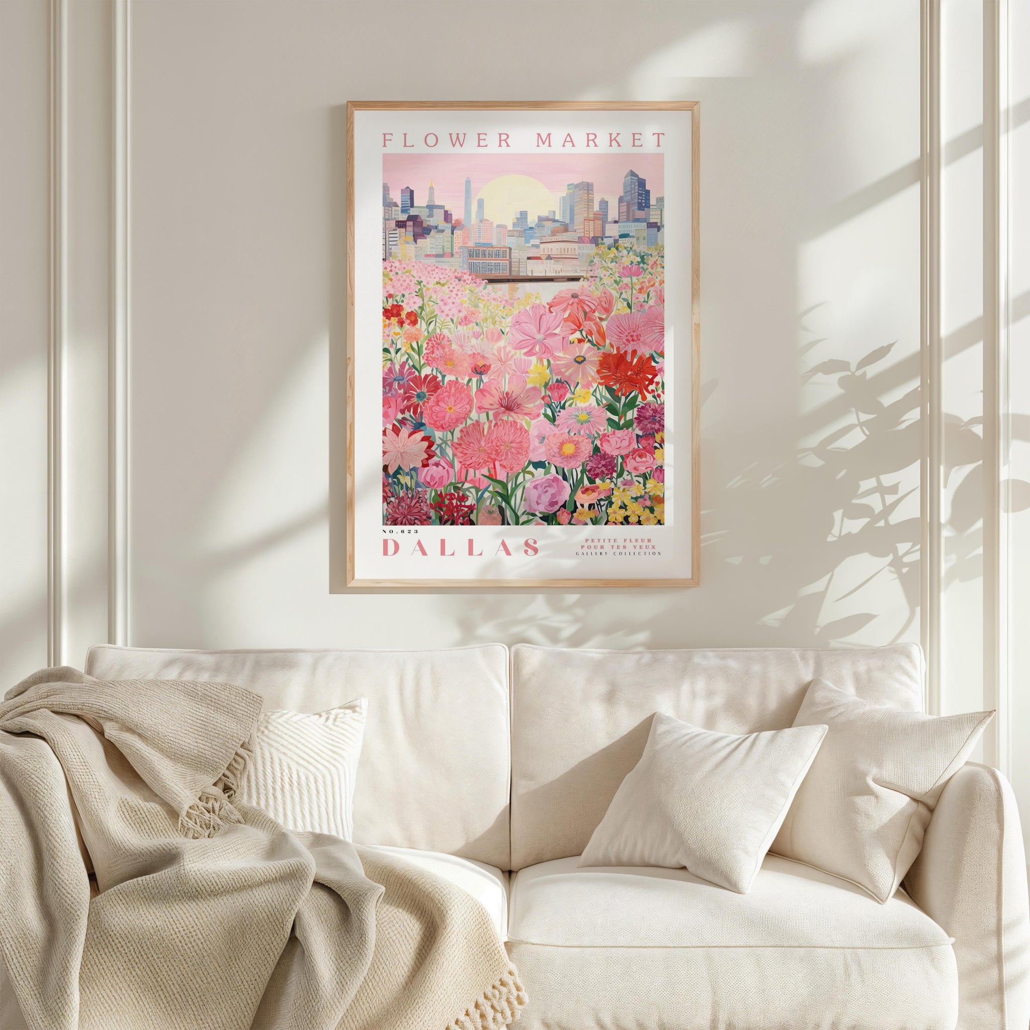 a framed poster of a cityscape with a field of flowers in the foreground, hanging on a wall above a white couch.